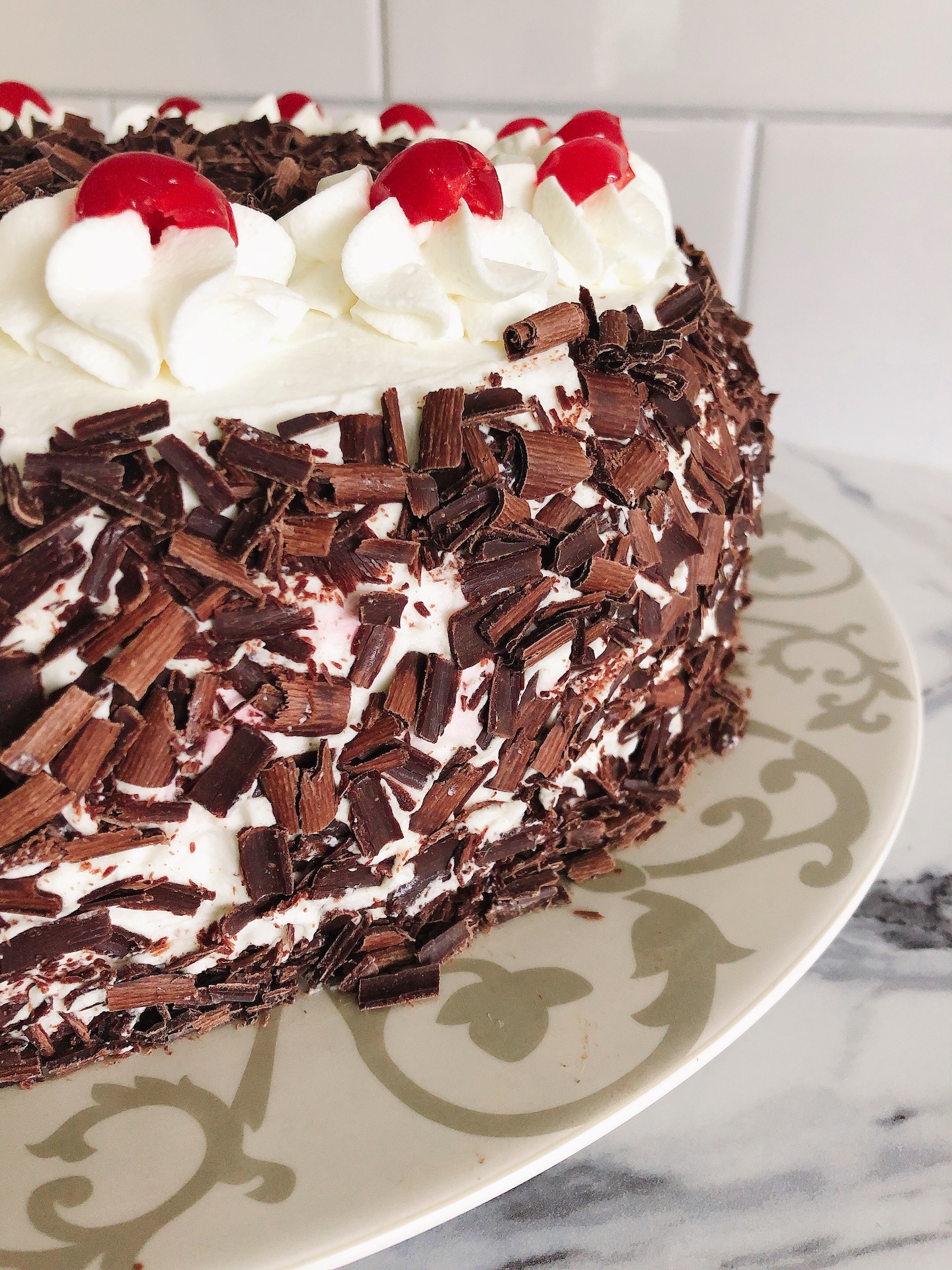 Side view of chocolate shavings and whipping cream florets with maraschino cherries on top of a black forest cake