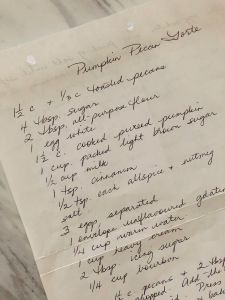 Handwritten recipe for a Pumpkin Pecan Torte on a plain piece of paper sitting on a white marble countertop