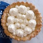 Banana Cream Pie with swirls of whipping cream on top of various sizes. A blue with white pattern tea towel lays underneath.