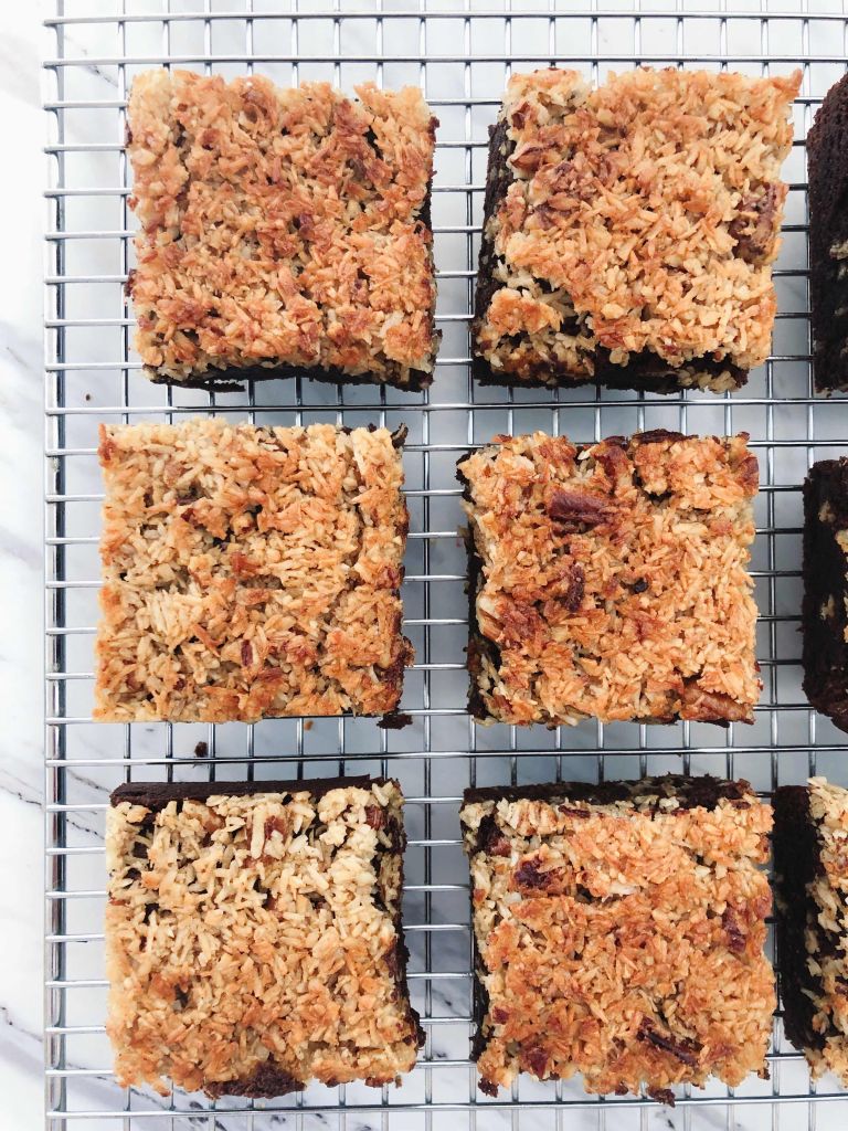 Six Whole Grain Rye Brownies with Toasted Coconut Pecan Topping lined up side by side on a cooling rack