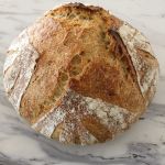 Golden brown loaf of spelt, einkorn and rye bread sitting on the countertop