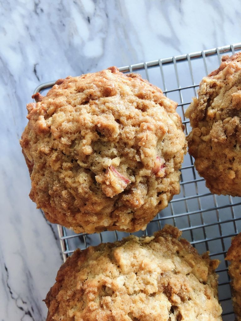 Close up of one lemon rhubarb spelt muffin with streusel on top surrounded up two other muffins all cooling on a wire rack