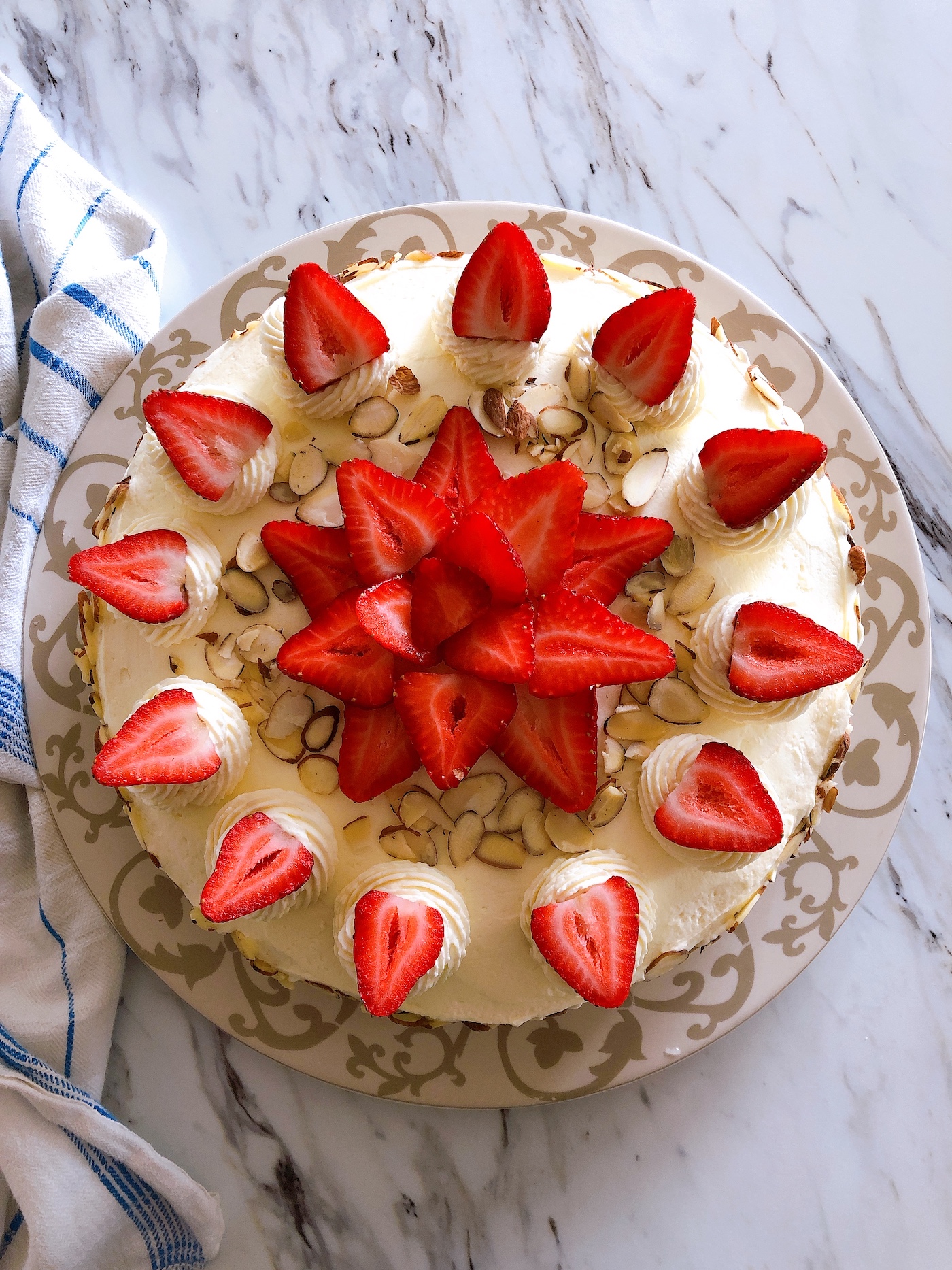 Top down view of a german buttercream spelt torte covered with sliced almonds and topped with swirls of buttercream and strawberries