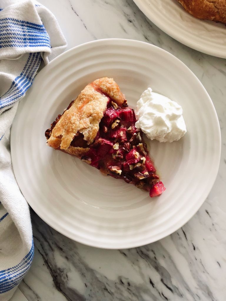 One slice of rhubarb pecan galette on a white plate with a dollop of whipped cream beside it.