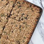 A baking sheet pan full of Homemade Chocolate Chip Granola Bars with Pumpkin, Sunflower and Sesame Seeds cut into thin rectangles on a white marble countertop.
