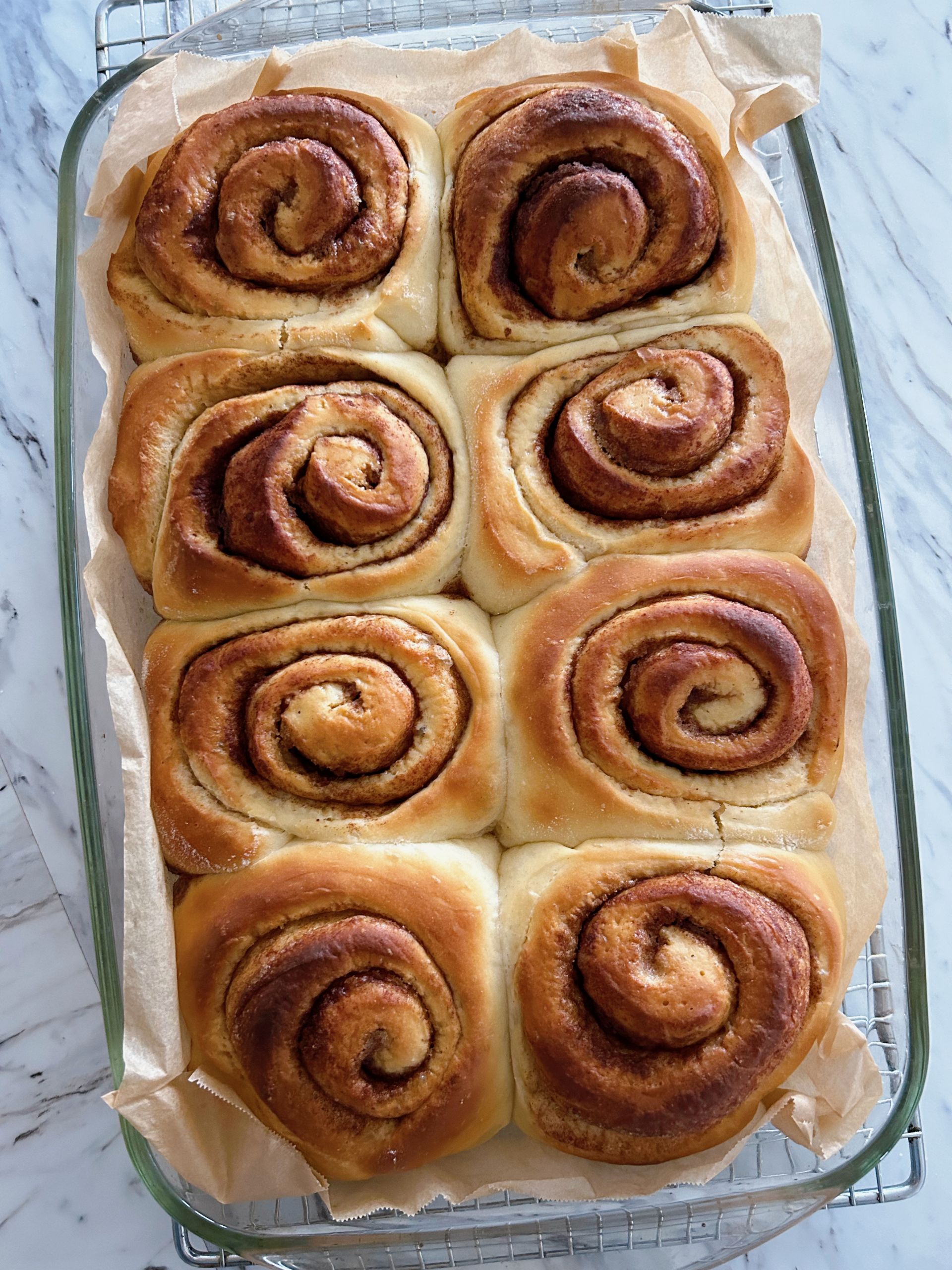 Eight large fluffy sourdough discard cinnamon buns cooling in a large baking dish.